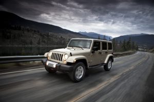 Grey 2018 Jeep Wrangler driving down the highway with a cloudy sky above.